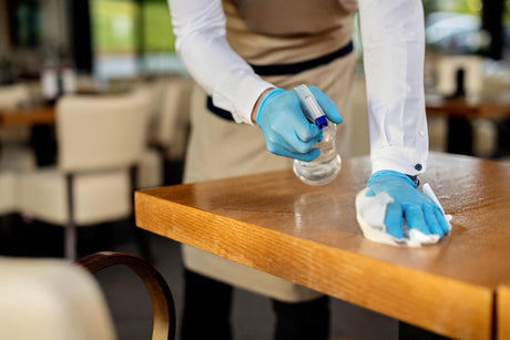"Person wiping down a kitchen trolley with a cloth and spray cleaner, showing steps for regular maintenance and hygiene."