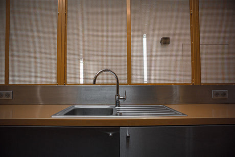 “Stainless steel kitchen sink being cleaned with a non-abrasive cleaner and soft cloth to remove water spots and restore shine.”