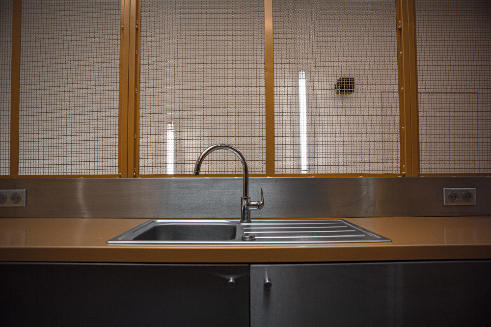 “Stainless steel kitchen sink being cleaned with a non-abrasive cleaner and soft cloth to remove water spots and restore shine.”