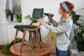 “Person reupholstering a dining chair by attaching new fabric over foam padding and securing it with a staple gun.”