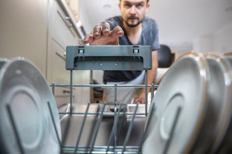 "Open modern dishwasher with energy-efficient and water-saving labels, loaded with neatly arranged dishes and utensils."