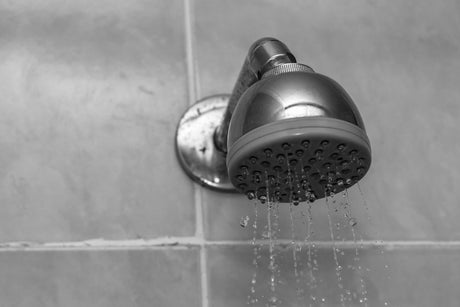 “Shower head wrapped in a plastic bag filled with vinegar, secured with a rubber band for hands-free cleaning without removal.”