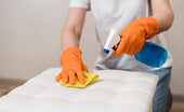 “Person spot-cleaning a mattress topper with a mild detergent and cloth to remove stains and freshen the surface.”