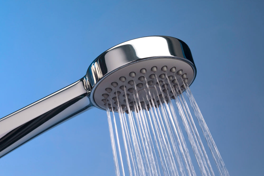 “Person cleaning a shower head with a vinegar-filled plastic bag secured around it to remove mineral buildup and restore water flow.”