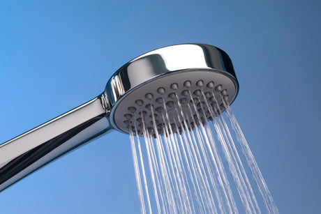 “Person cleaning a shower head with a vinegar-filled plastic bag secured around it to remove mineral buildup and restore water flow.”
