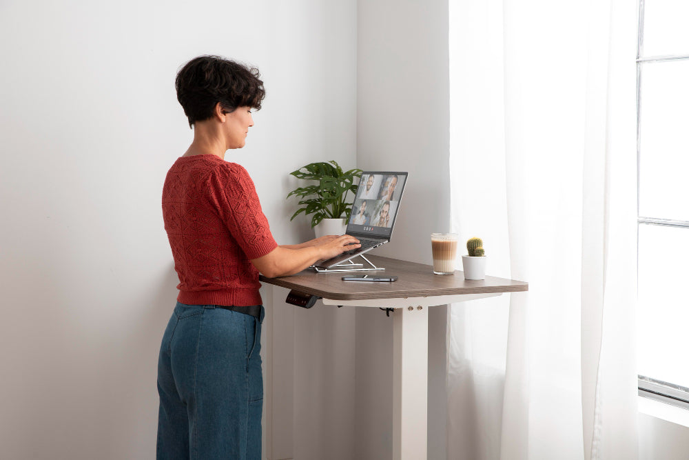 “Person pressing and holding the reset button on an electric standing desk control panel to recalibrate its height settings.”