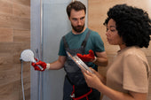 “Person installing a frameless glass shower screen by aligning it with wall brackets and securing it with a drill.”