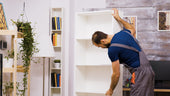 “Person installing a floating shelf on a wall using a level, drill, and concealed mounting bracket for a seamless finish.”