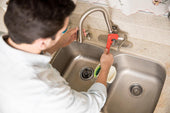 “Person using a plunger on a kitchen sink to remove a clog and restore proper drainage.”