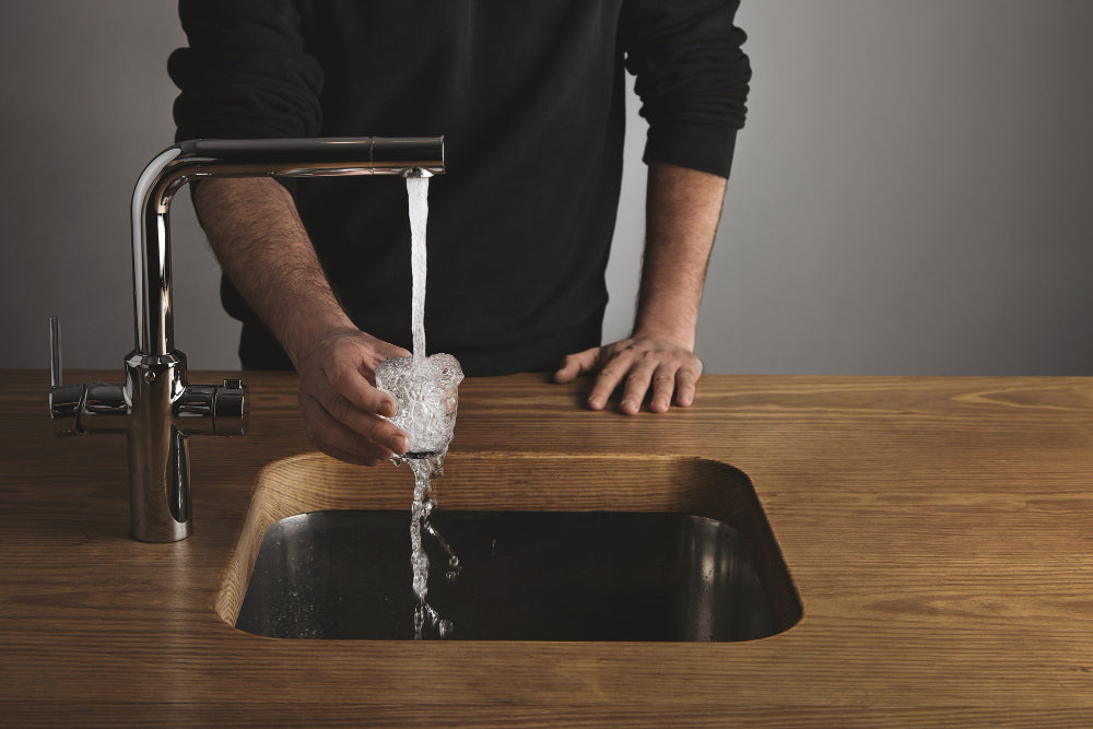 “Person pouring baking soda and vinegar into a kitchen sink drain to clean it naturally and remove odors.”