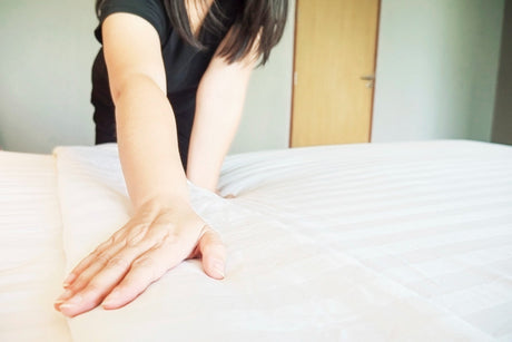 "Person rotating a king size mattress in a bright bedroom, showing care practices like flipping, airing, and using a protective cover for durability."