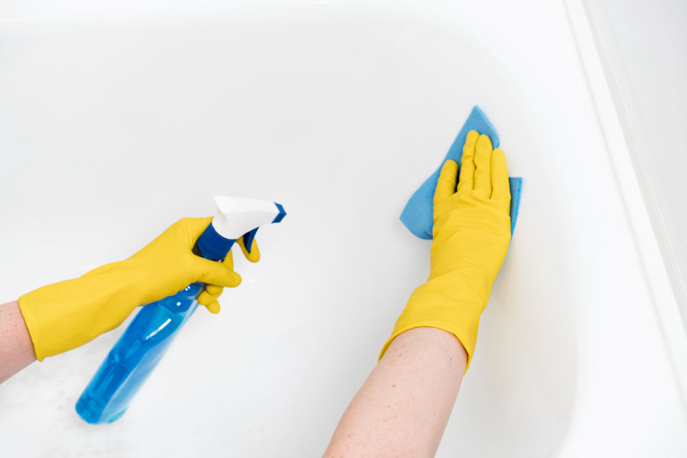 "Person cleaning a bathtub with a sponge and spray bottle, showing effective bathtub cleaning techniques."