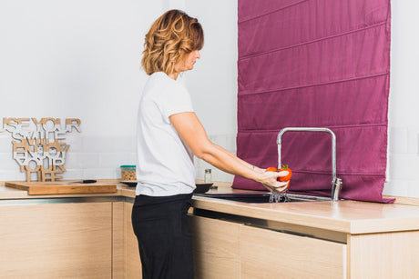 "Person scrubbing a kitchen sink with a sponge and cleaner, showing effective daily maintenance for a spotless finish."