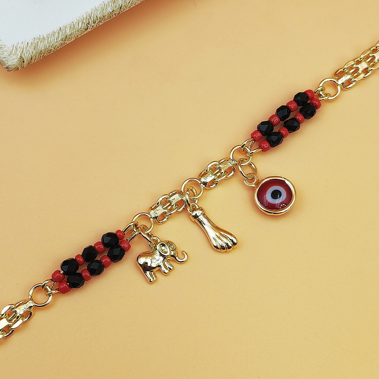 Gold-Tone Chain Bracelet with Red and Black Beads, Elephant Charm, Feather Pendant, and Round Stone Accent – 19 cm Length